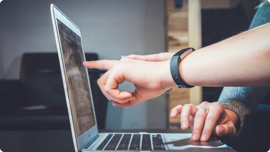 Pessoa digitando em um teclado de notebook com gráficos na tela, um óculos escuro ao seu lado, junto com um celular